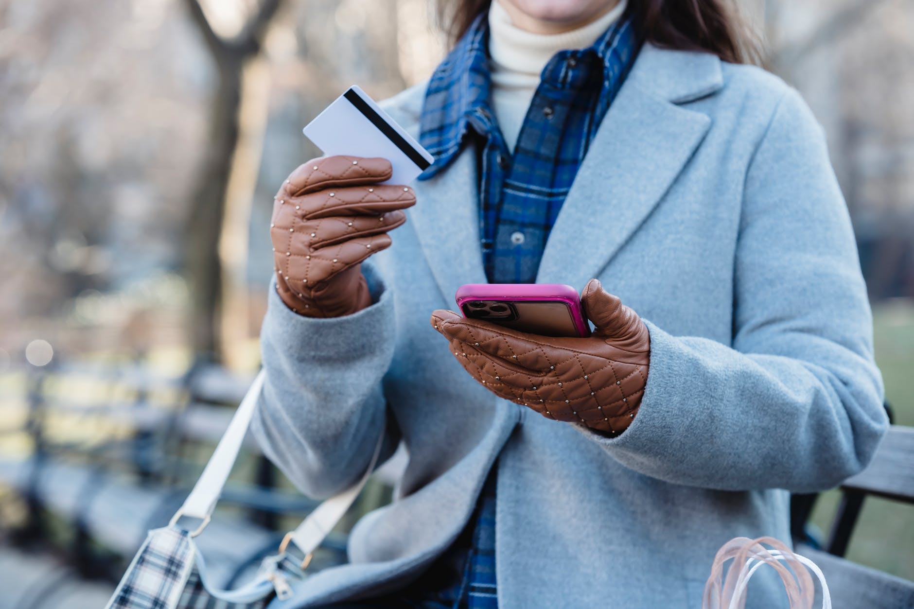 woman using smartphone and holding credit card while sitting in park